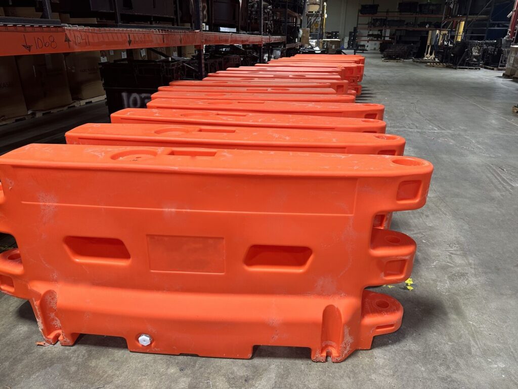 orange construction barriers made via rotomolding lined up in a warehouse